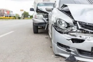 Two cars with significant front-end damage after a rear-end collision on a road, with debris visible and no people present.
