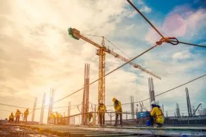 Construction workers on a building site with a large crane in the background, silhouetted against a partly cloudy sky.