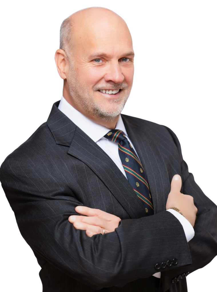 Bald man in a suit and tie stands with arms crossed, smiling at the camera against a plain white background.