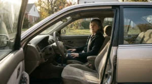 woman seated in driver's seat of parked sedan with open door